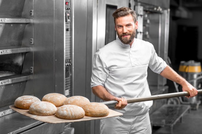 Baker taking out from the oven baked buckweat bread